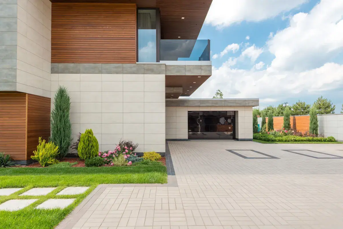 A modern minimalist house with a spacious driveway and landscaped garden under a clear blue sky.