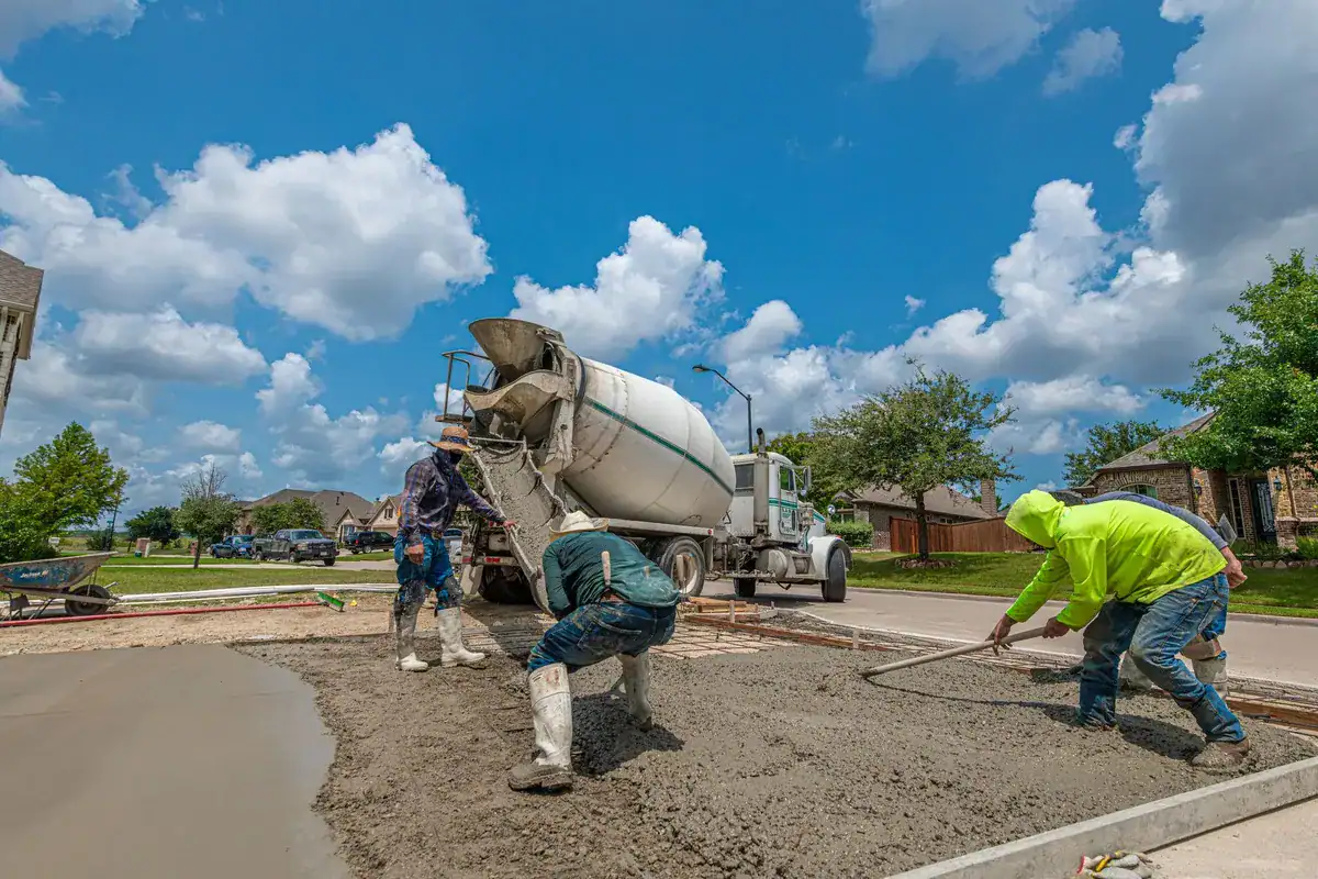 Construction workers pouring concrete for a driveway under a clear blue sky, highlighting proper maintenance.